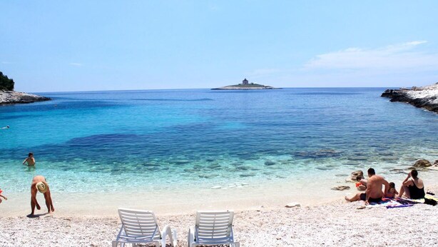 A beach with clear turquoise water, a small island in the distance, and people relaxing on the sand. - Hotel Teranea (Hvar)