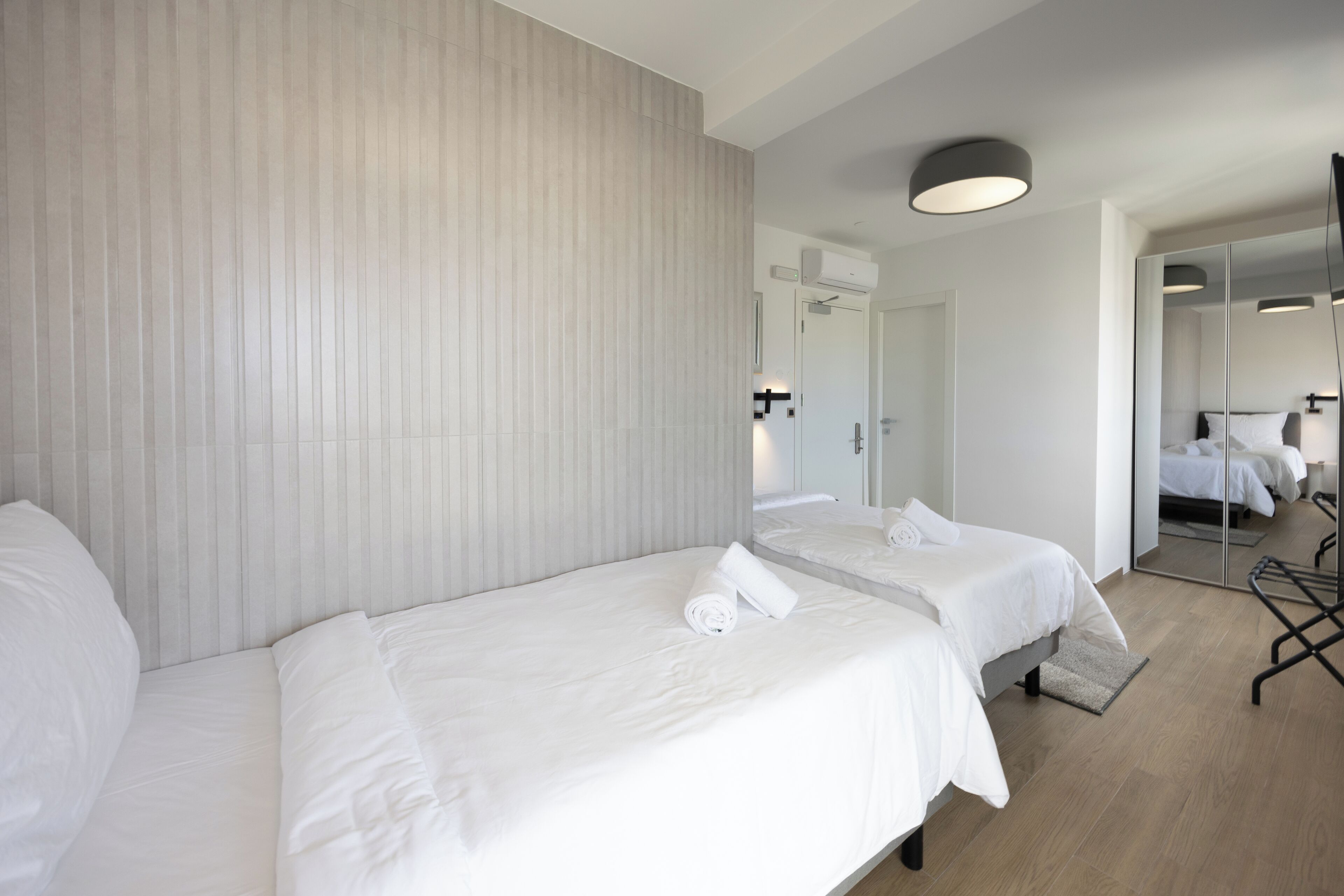 Une chambre d’hôtel avec deux lits simples, un grand miroir et un luminaire moderne.