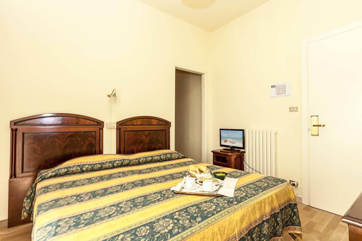 Una camera d'albergo con un letto, una televisione e un vassoio con prodotti per la colazione.