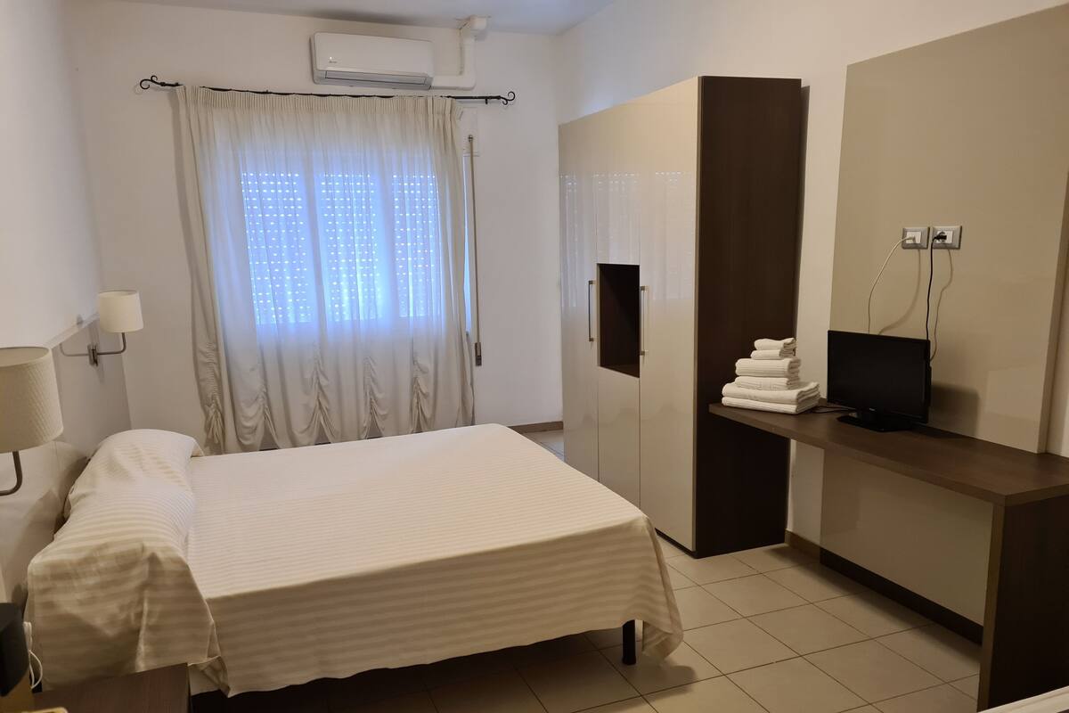 Una camera d'albergo con un letto, una scrivania con televisore, un armadio e una finestra con tende.