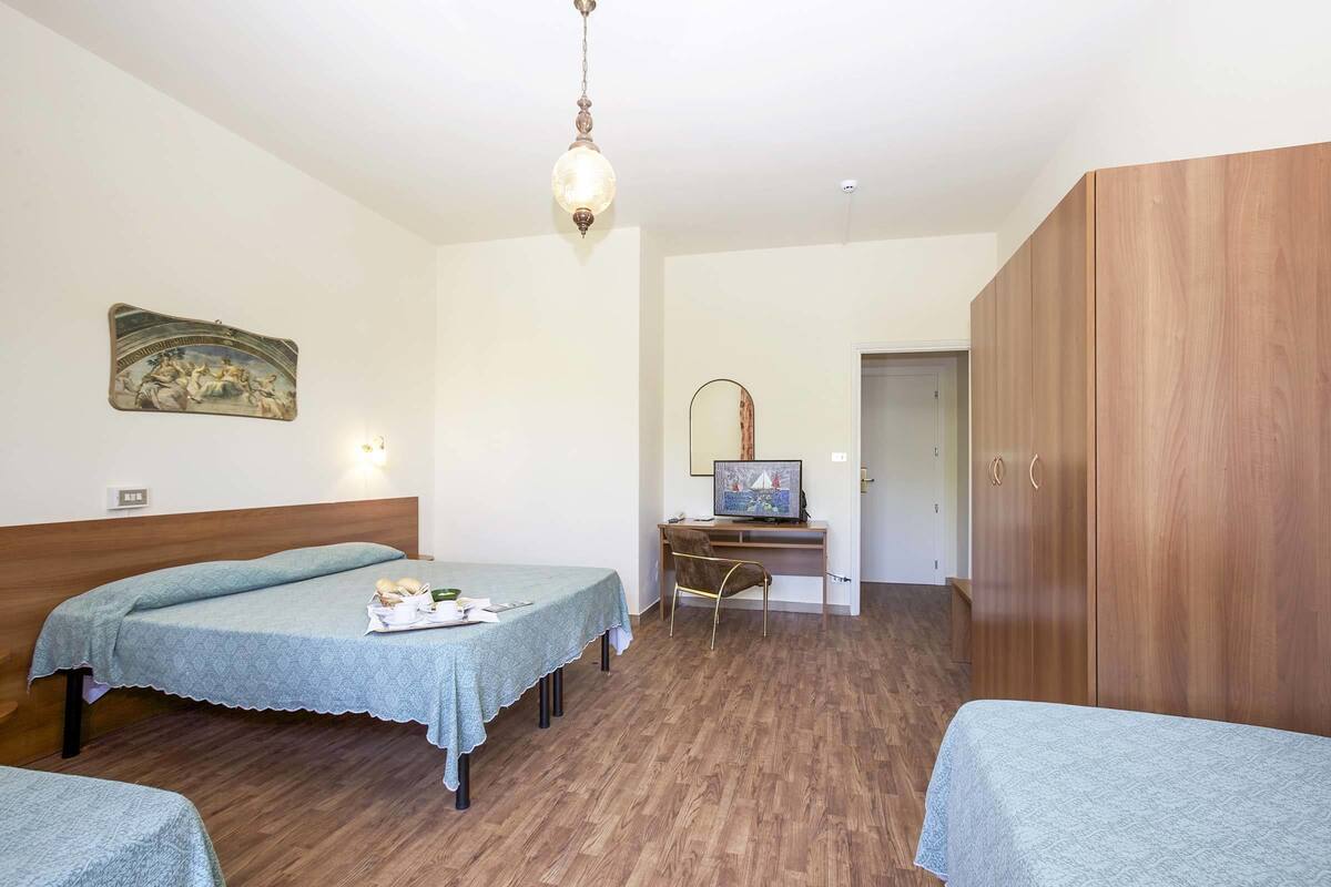 Una stanza con due letti, una scrivania con un computer, un armadio in legno e un quadro appeso al muro.