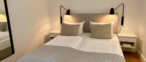 A neatly made bed with a checkered bedspread and pillows, two bedside tables with lamps, and a mirror on the left wall.