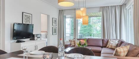 A modern living room with a dining area, a flat-screen TV, and a sofa with plaid cushions.