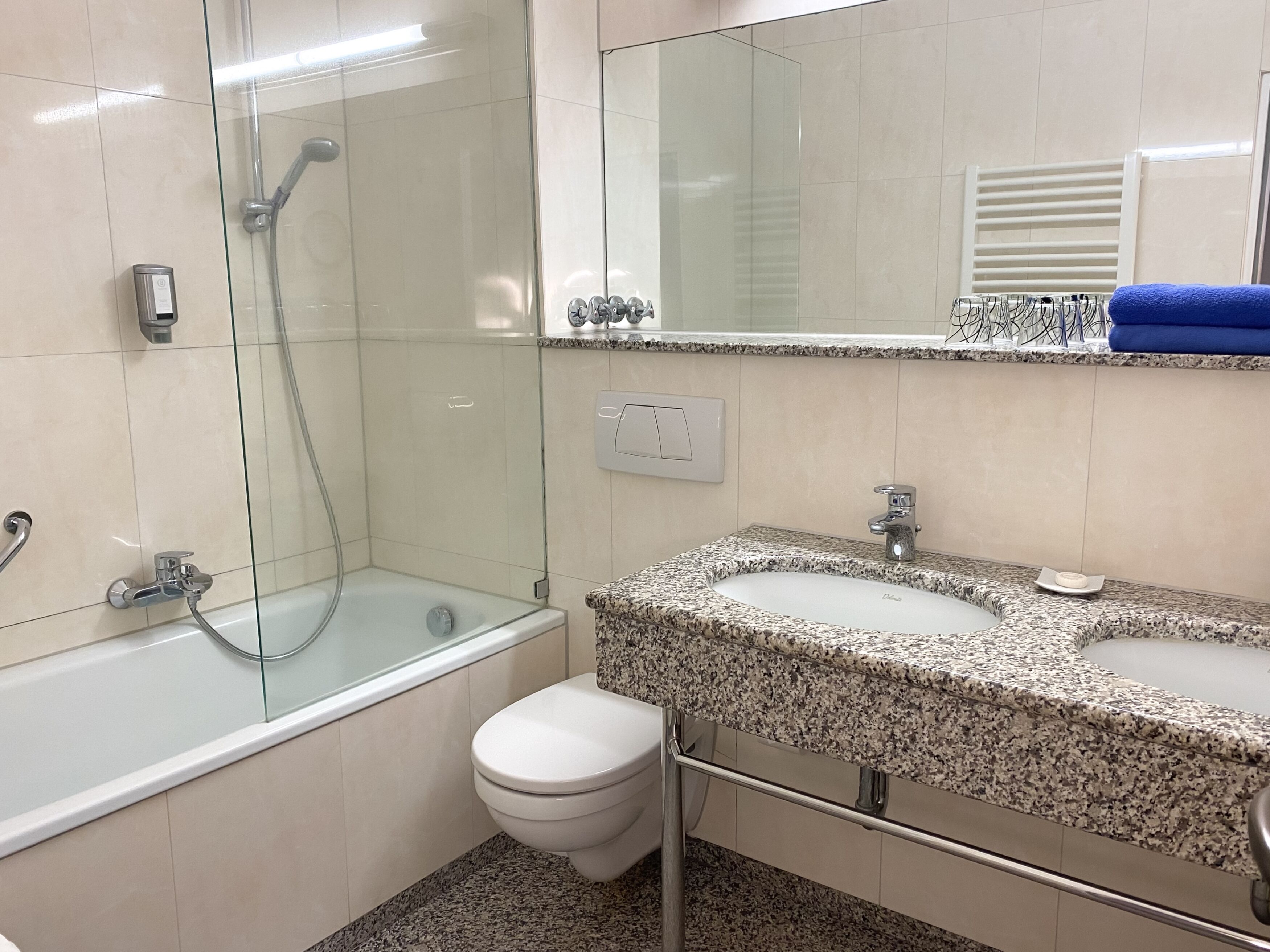 Casa de banho moderna com chuveiro em cabine de vidro, sanita branca e lavatório com bancada de granito.