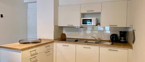 A compact kitchen with white cabinets, a microwave, a coffee maker, and a sink.