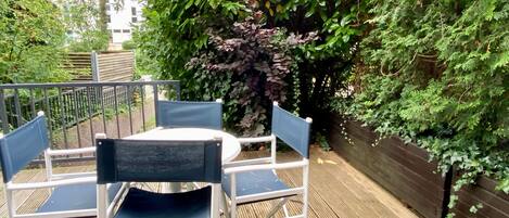 An outdoor patio with a round table and four chairs, surrounded by lush greenery and a wooden fence.