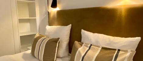 A neatly made bed with striped pillows and a headboard, two bedside lamps, and a white shelving unit.