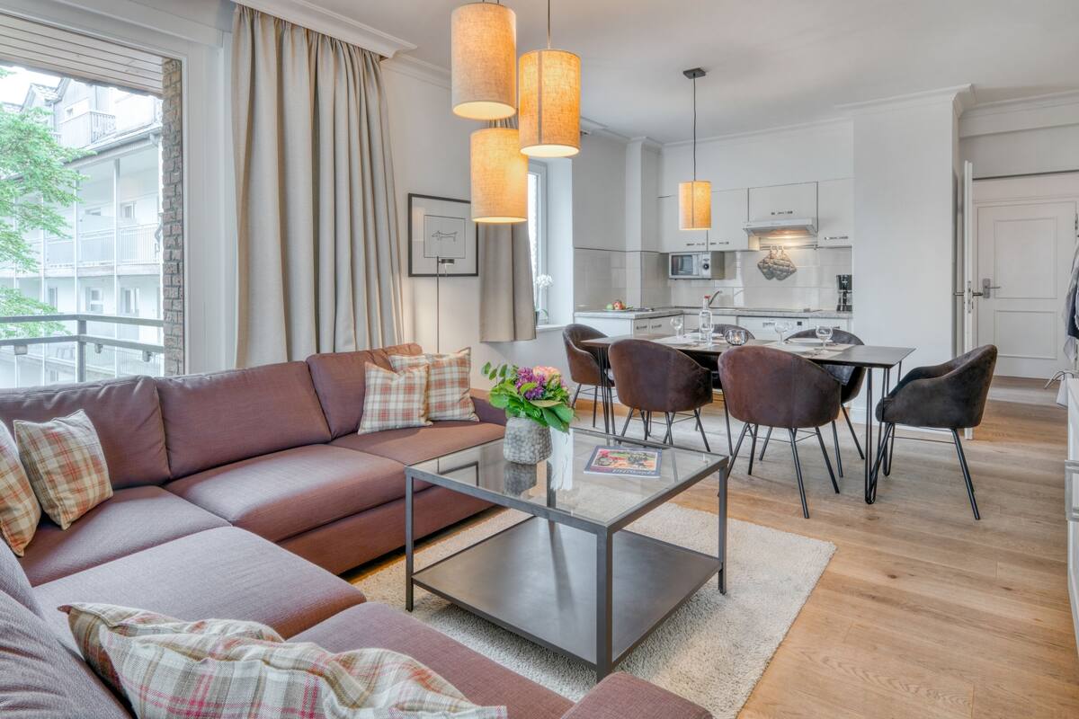 A modern living room with a sofa, a glass coffee table, and a dining area with chairs and a table.
