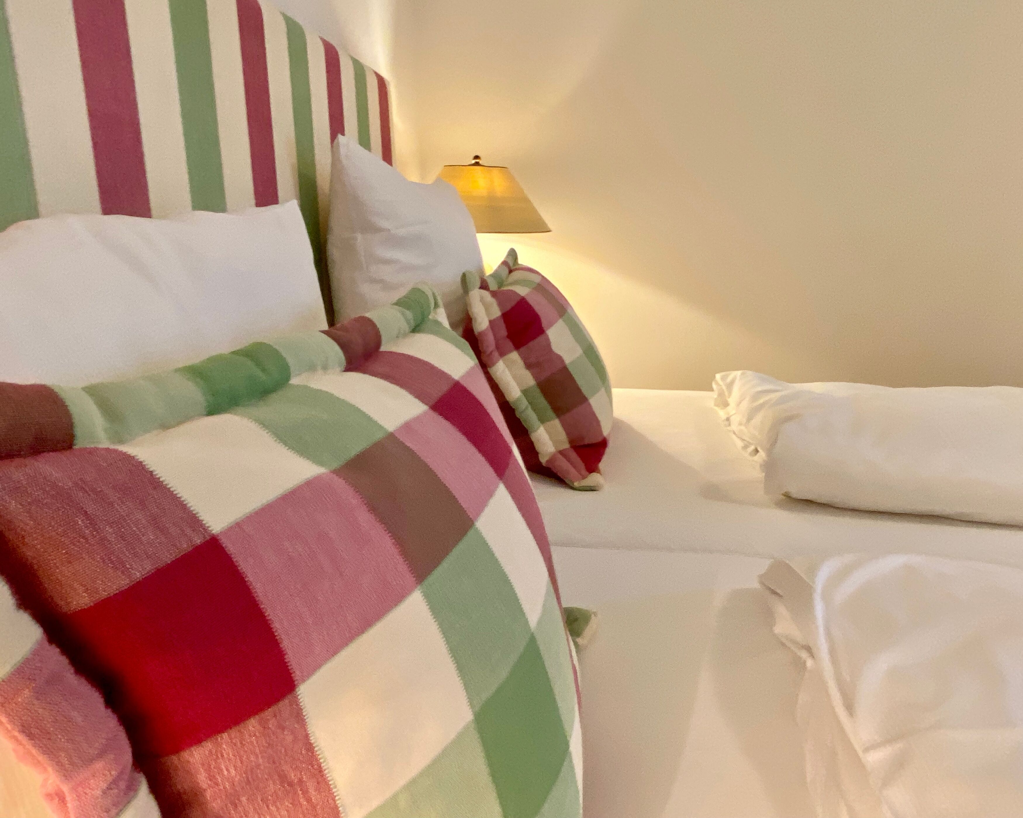 A hotel room with a bed covered in a checkered blanket, pillows, and a neatly made bed with white linens.