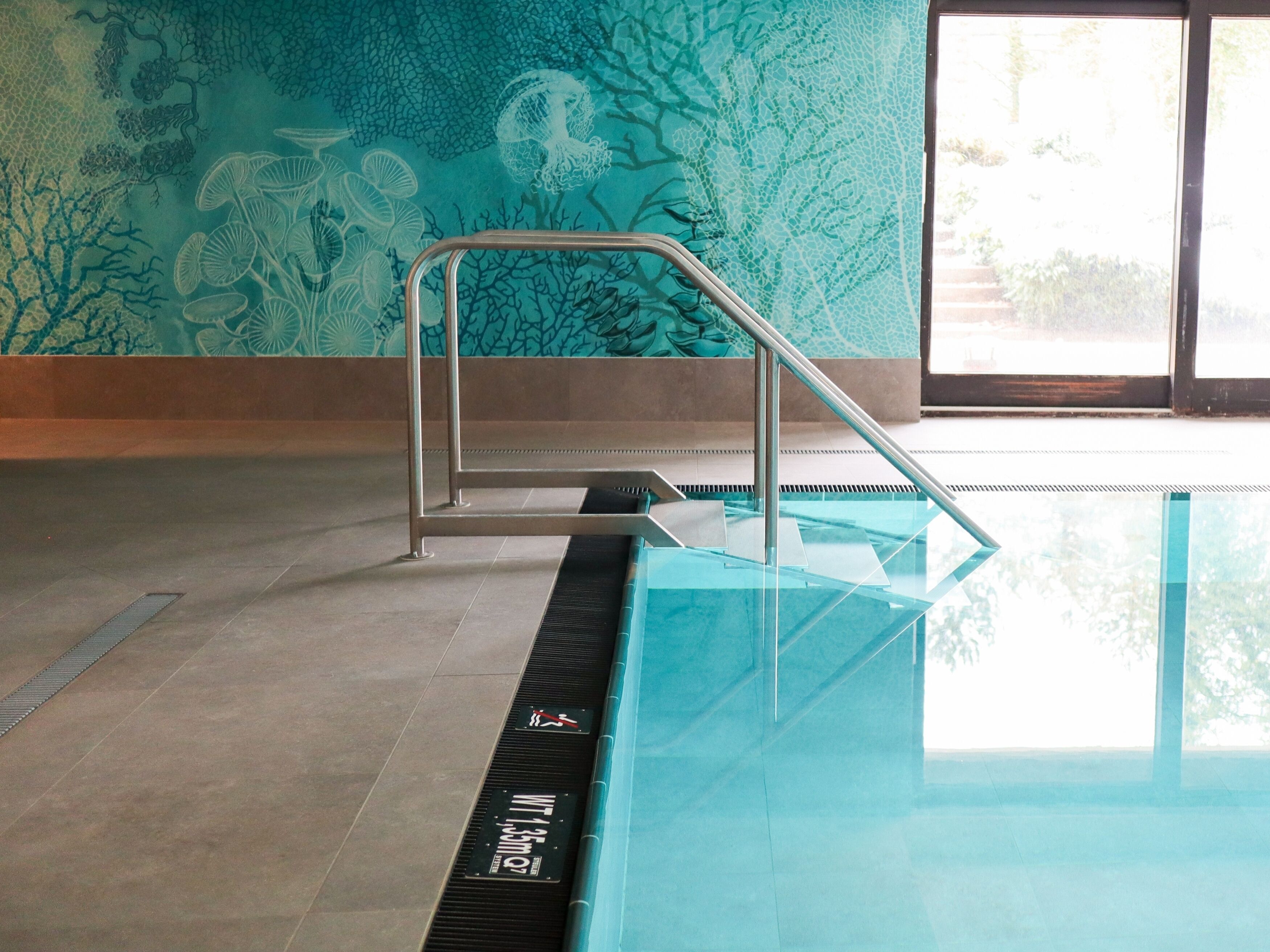 A swimming pool with a glass barrier and a tiled floor.