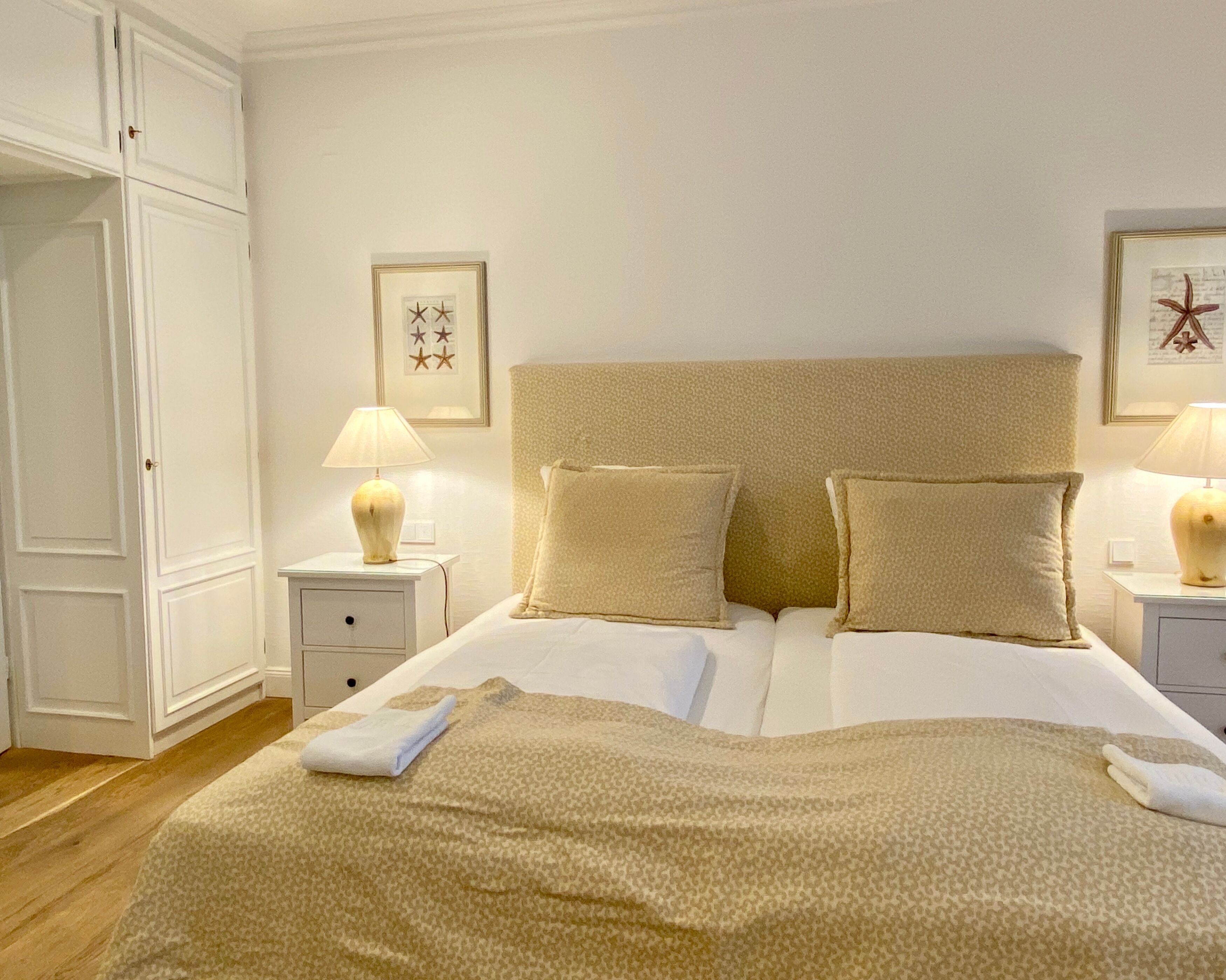Una cama bien hecha con dos almohadas, una mesita de noche con lámpara y un armario.