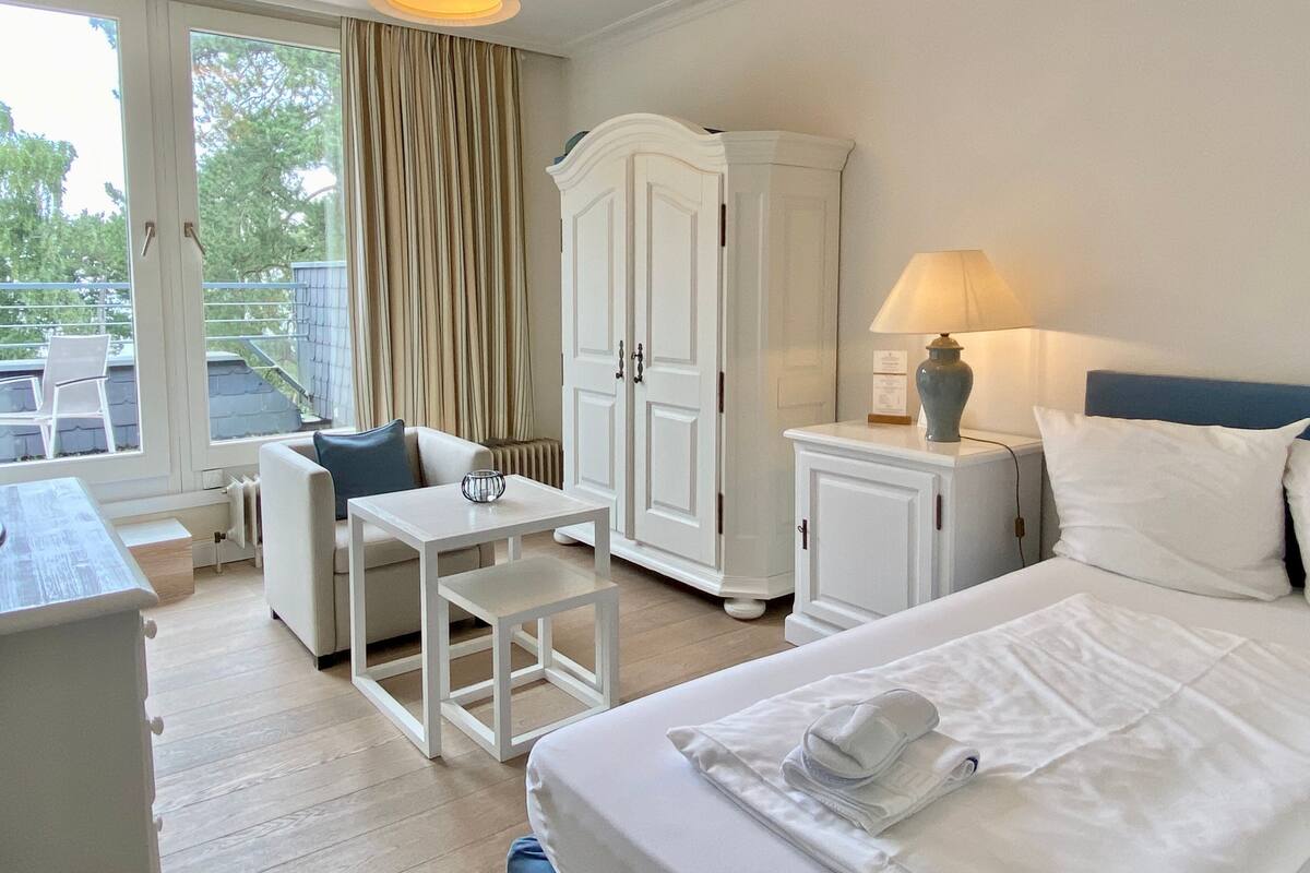 A hotel room with a bed, a desk, a chair, a wardrobe, and a lamp.