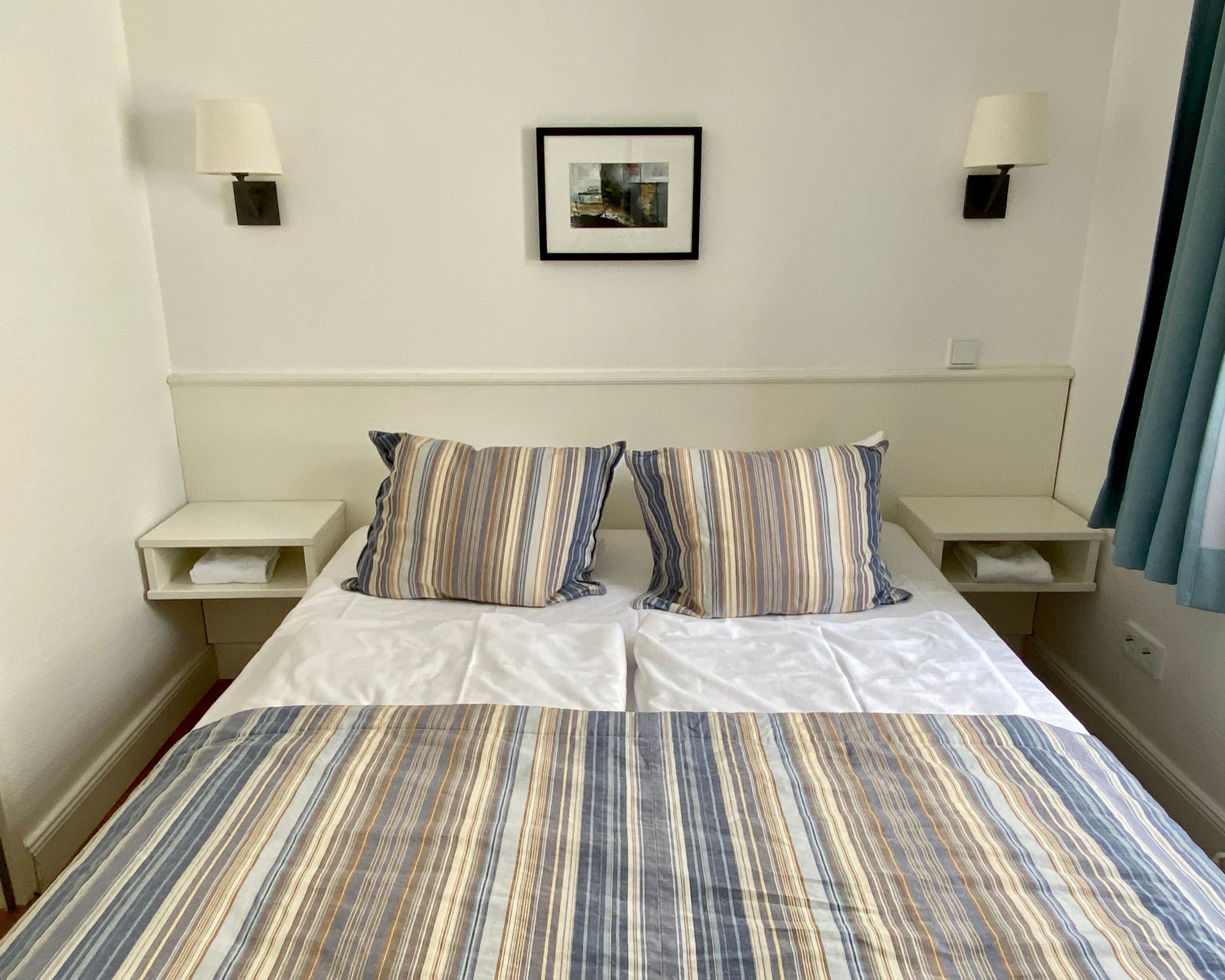 A hotel room with a large bed, striped bedding, two bedside tables with lamps, and a framed picture on the wall.