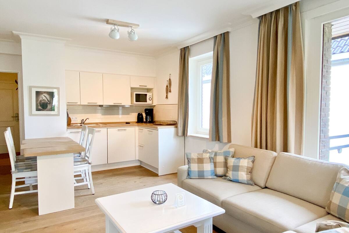A compact living space with a kitchenette, a dining area, and a sofa with plaid cushions.