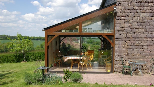 Een glazen patio met tuinmeubilair, een stenen muur en uitzicht op een groen landschap.