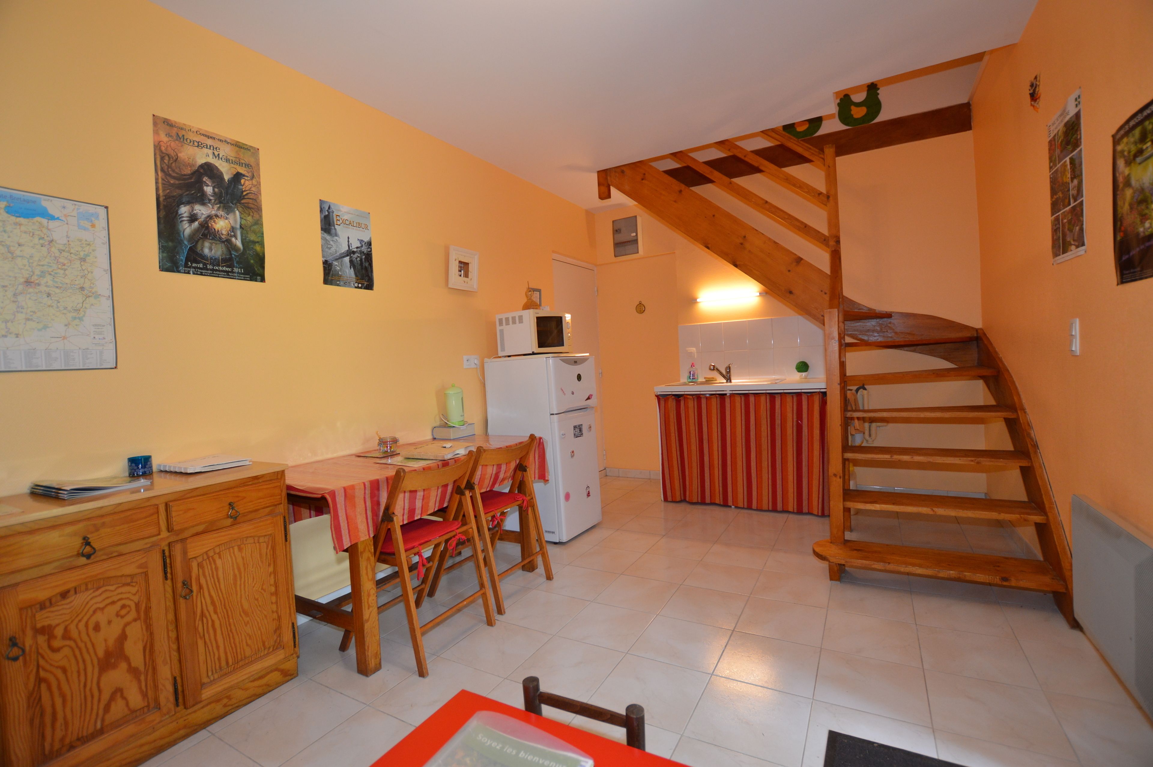 A compact kitchen with a wooden staircase, a dining area with a table and chairs, and a refrigerator.