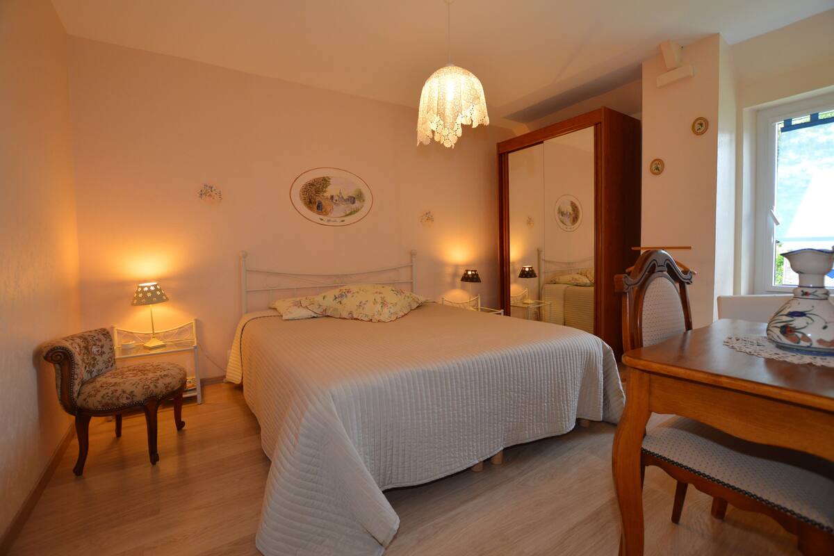 Une chambre à coucher avec un lit, une chaise, une table, une lampe et un miroir.