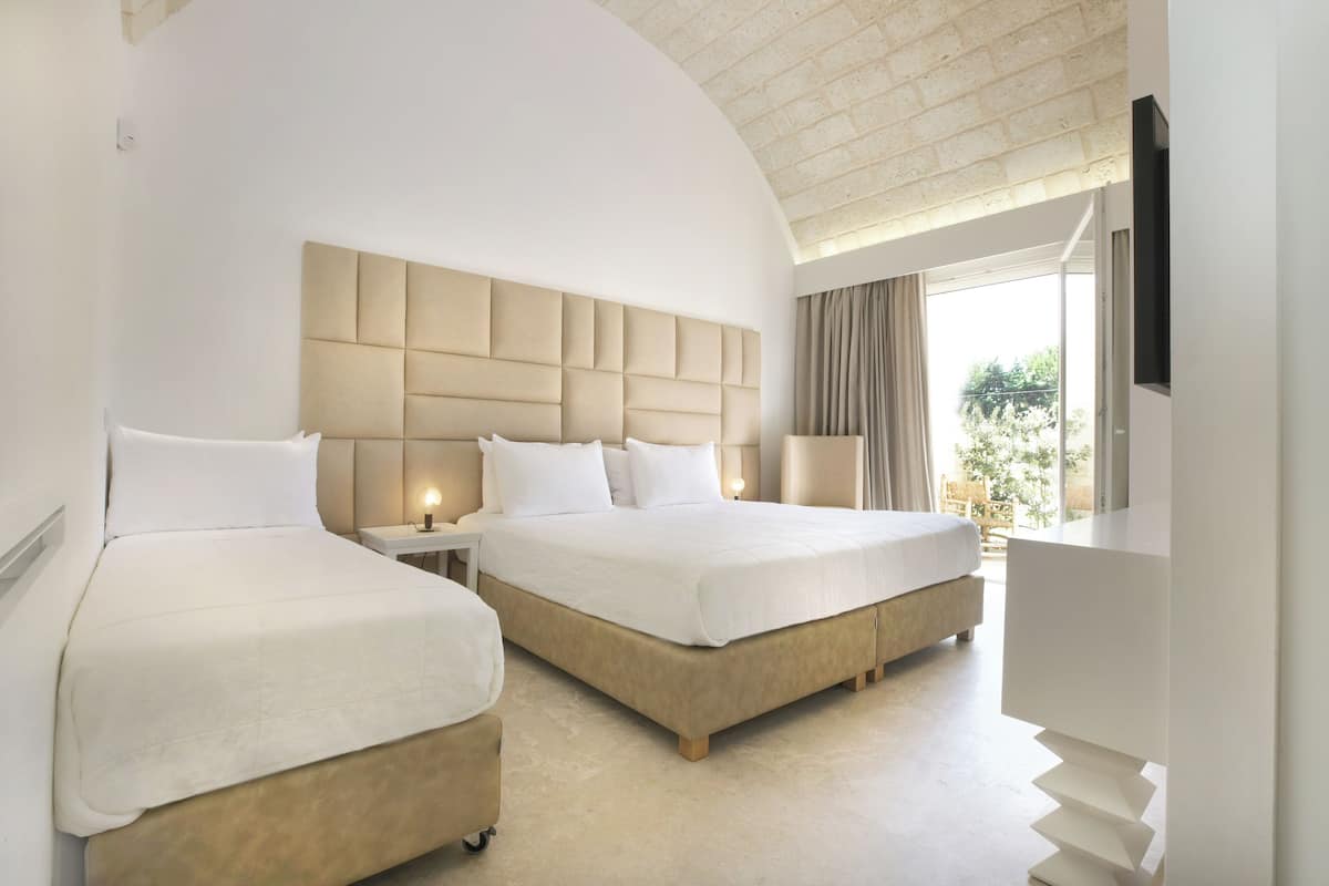 Een hotelkamer met twee bedden, een groot hoofdeinde, een televisie en een raam met gordijnen.