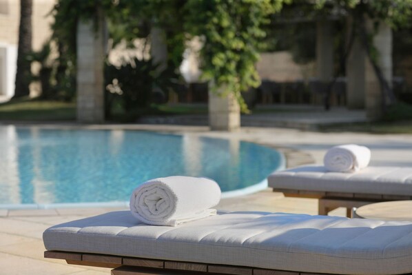 Un área de descanso junto a la piscina con sillas blancas acolchadas y una toalla blanca enrollada.