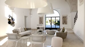A spacious living room with a white sofa, wicker chairs, a round coffee table, and a large white pendant light. - Masseria Antonio Augusto (Leverano)
