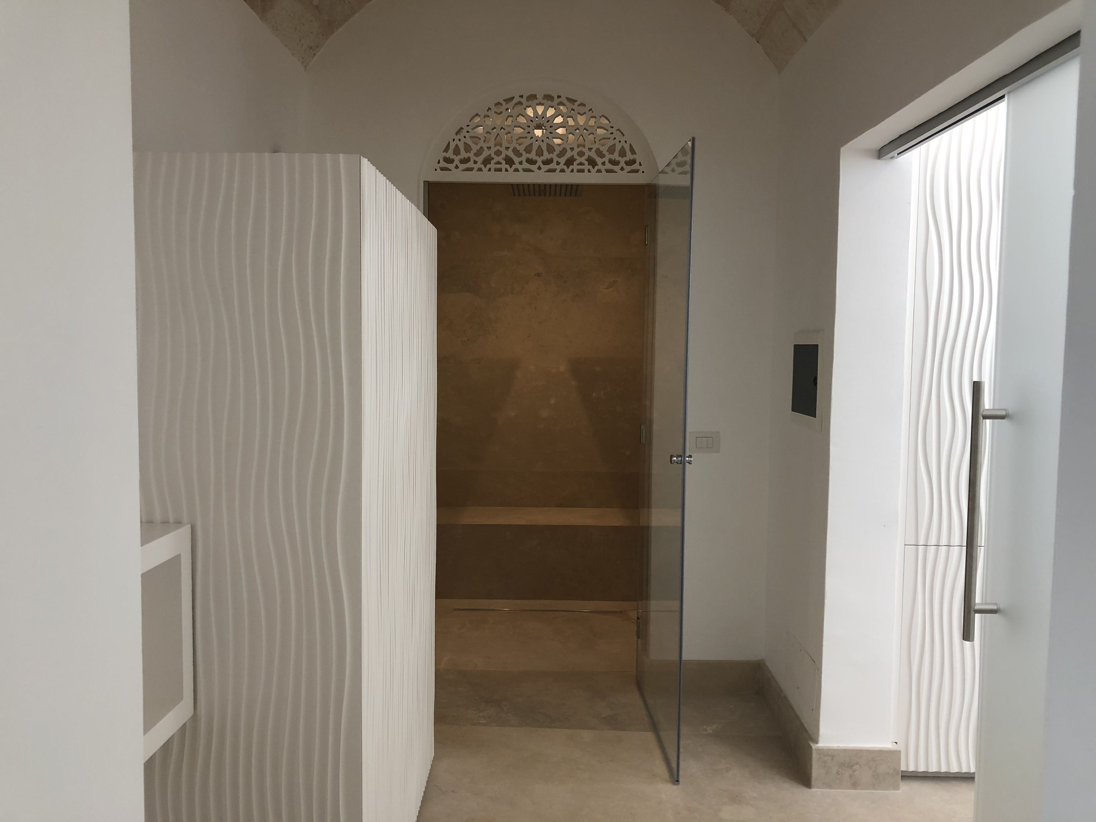Un baño moderno con puerta de vidrio para la ducha, pared con textura e iluminación empotrada en el techo.