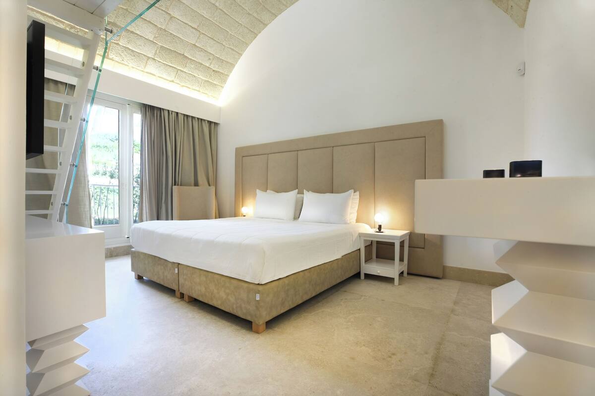 Een moderne slaapkamer met een groot bed, een nachtkastje, een inbouwbank en een trap.