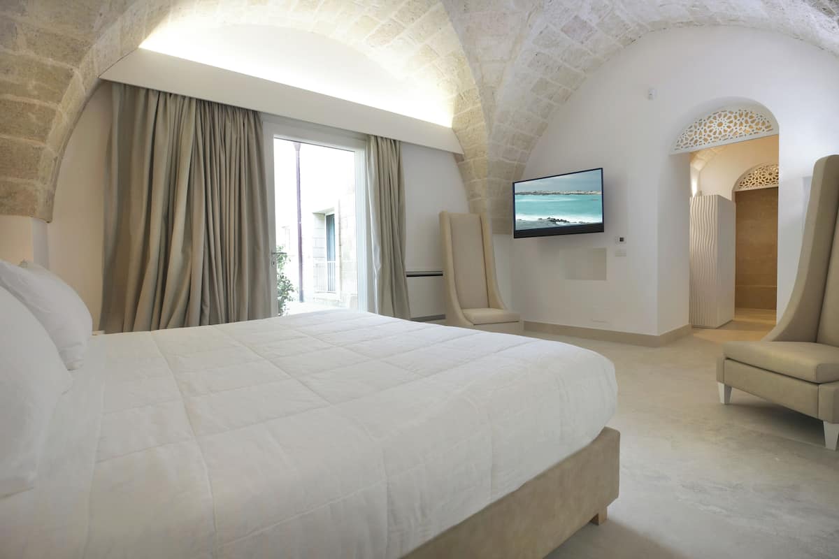 Een ruime slaapkamer met een groot bed, een flatscreen televisie aan de muur en uitzicht op zee.