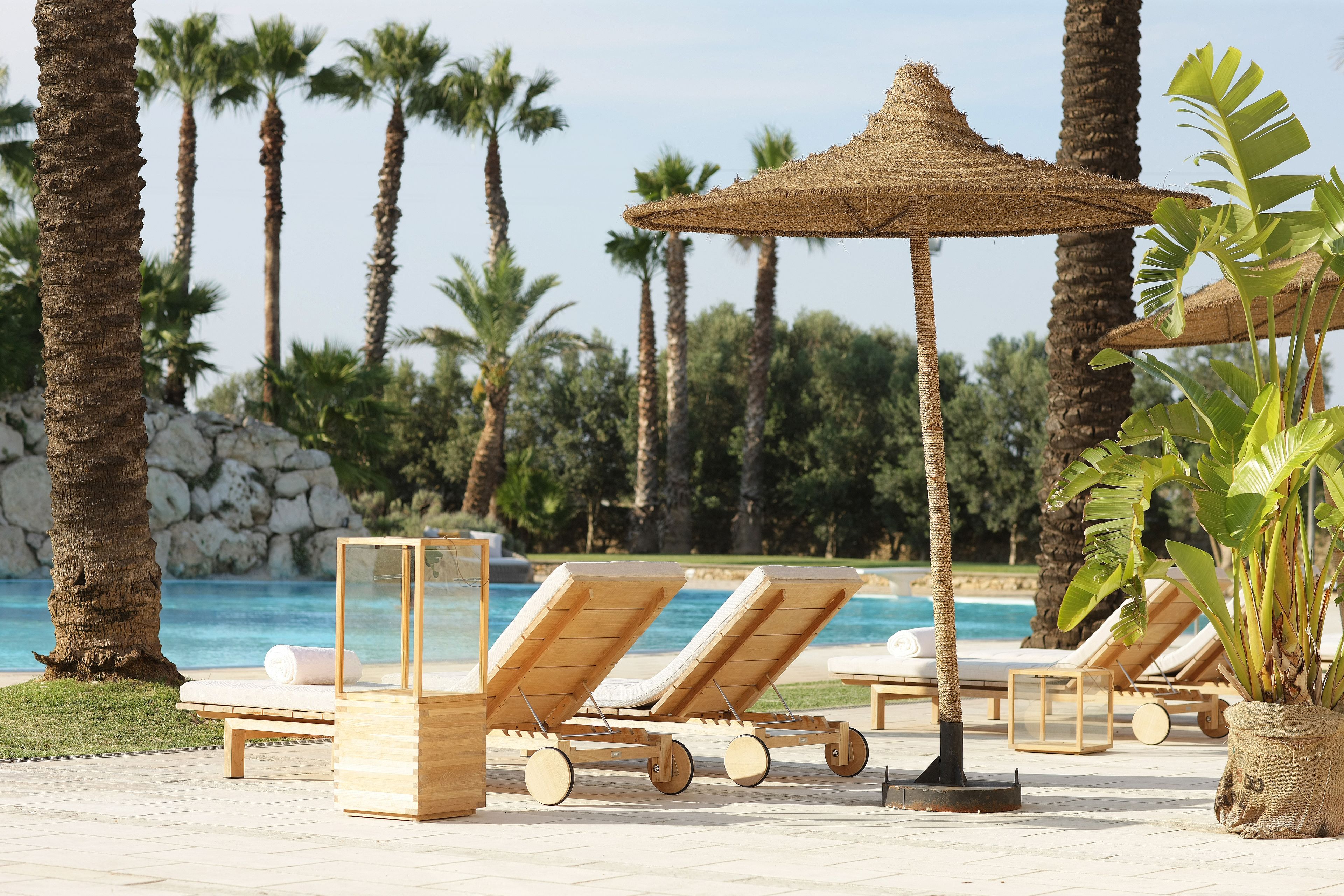 A poolside area with lounge chairs and a thatched umbrella.