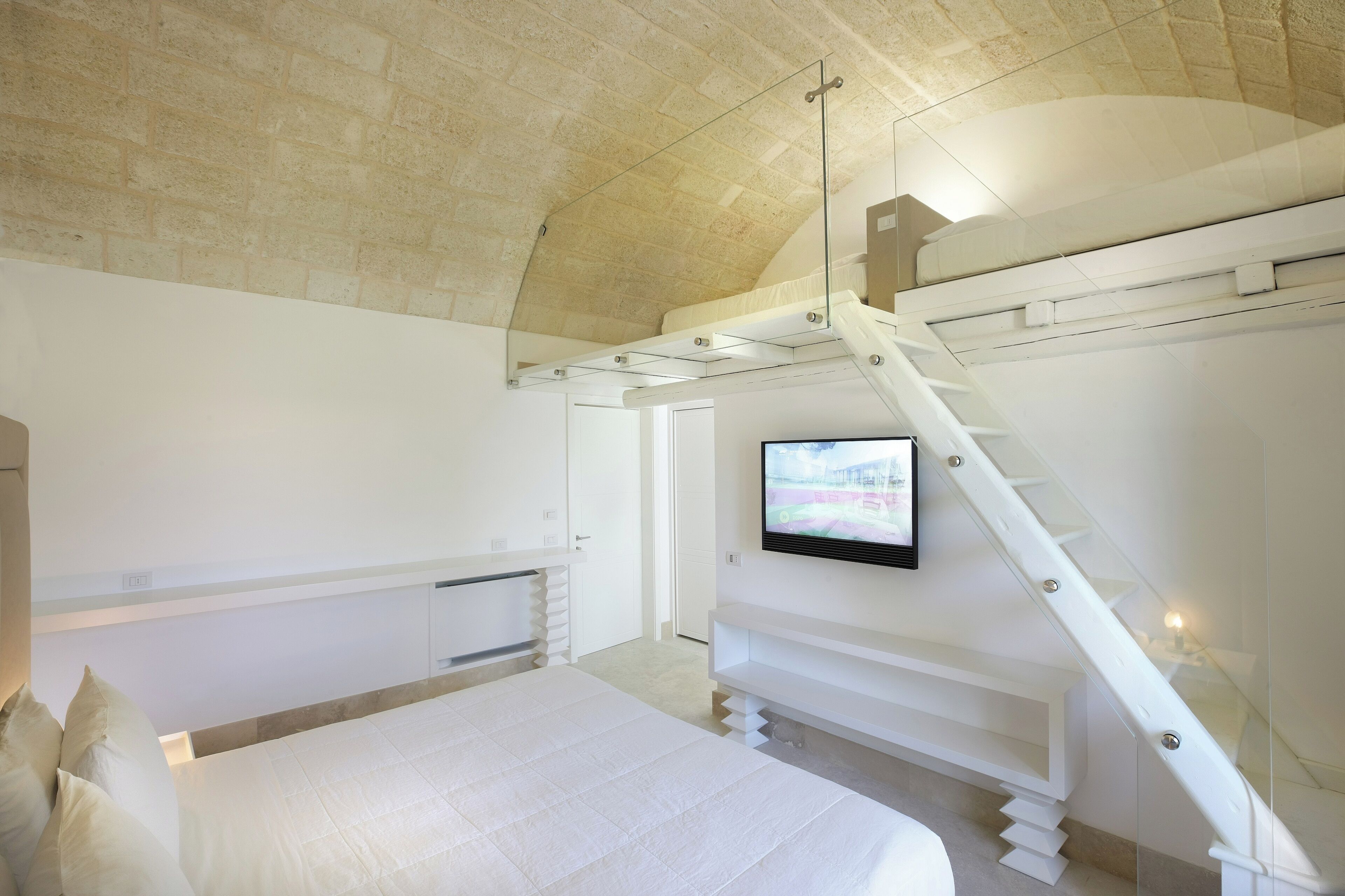 Quarto com cama, televisão fixada na parede e escada.