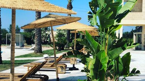 A courtyard with thatched umbrellas, lounge chairs, and potted plants. - Masseria Antonio Augusto (Leverano)