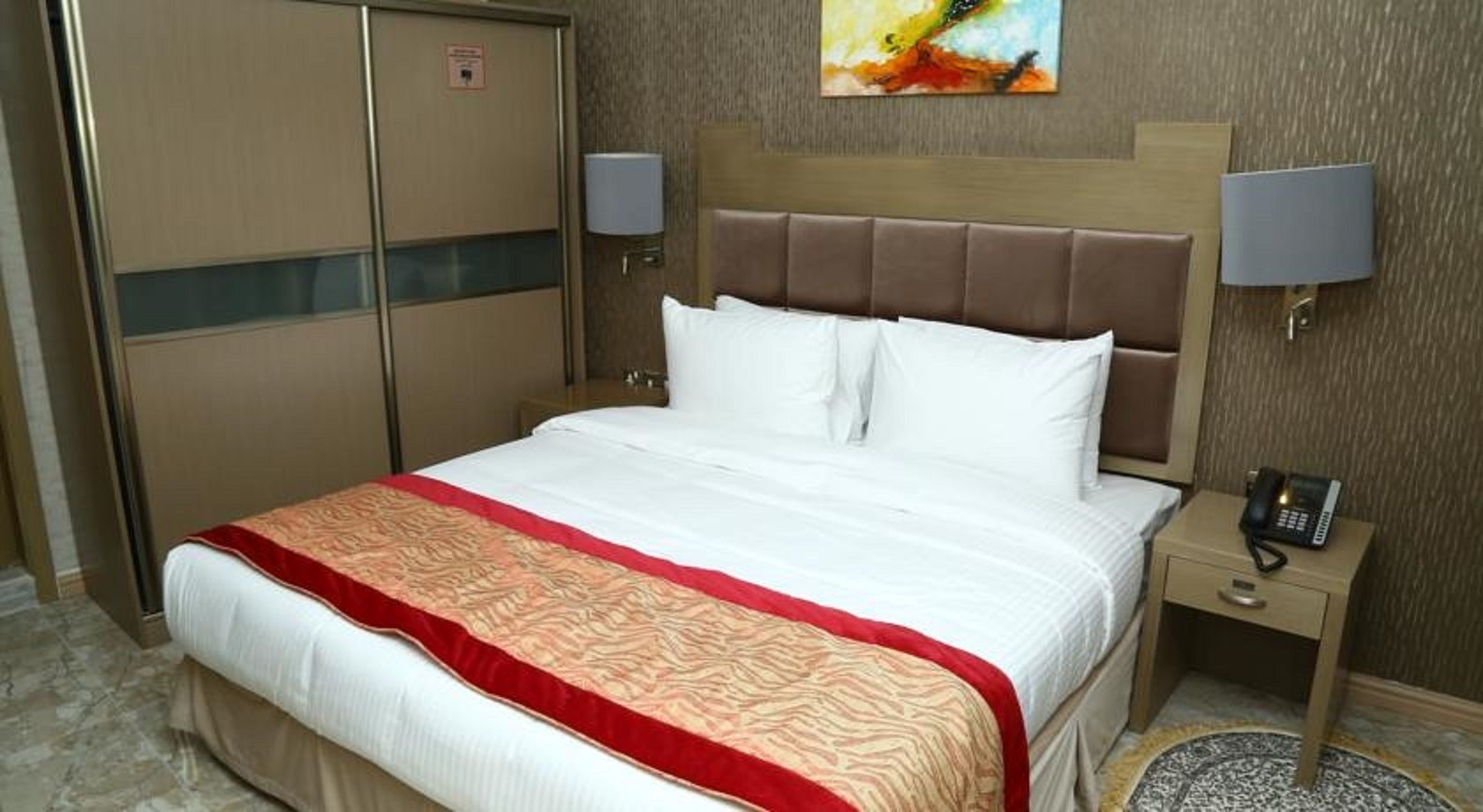A hotel room with a bed, a nightstand with a phone, and a door with a sign.