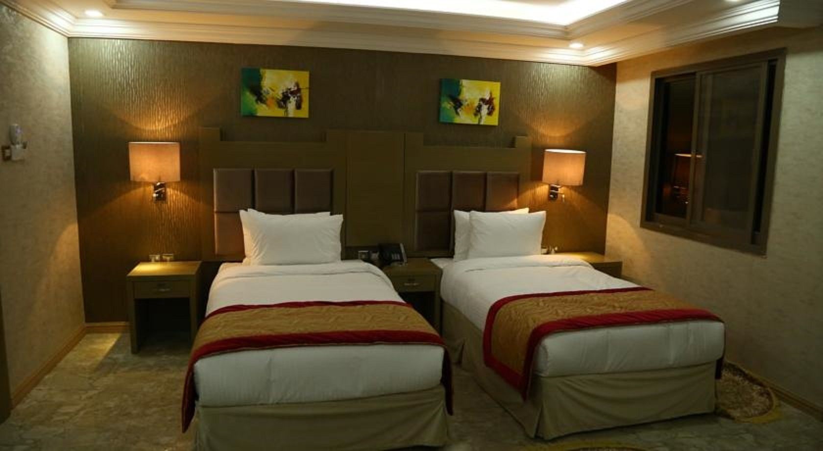 A hotel room with two beds, a headboard, nightstands, and wall-mounted lamps.