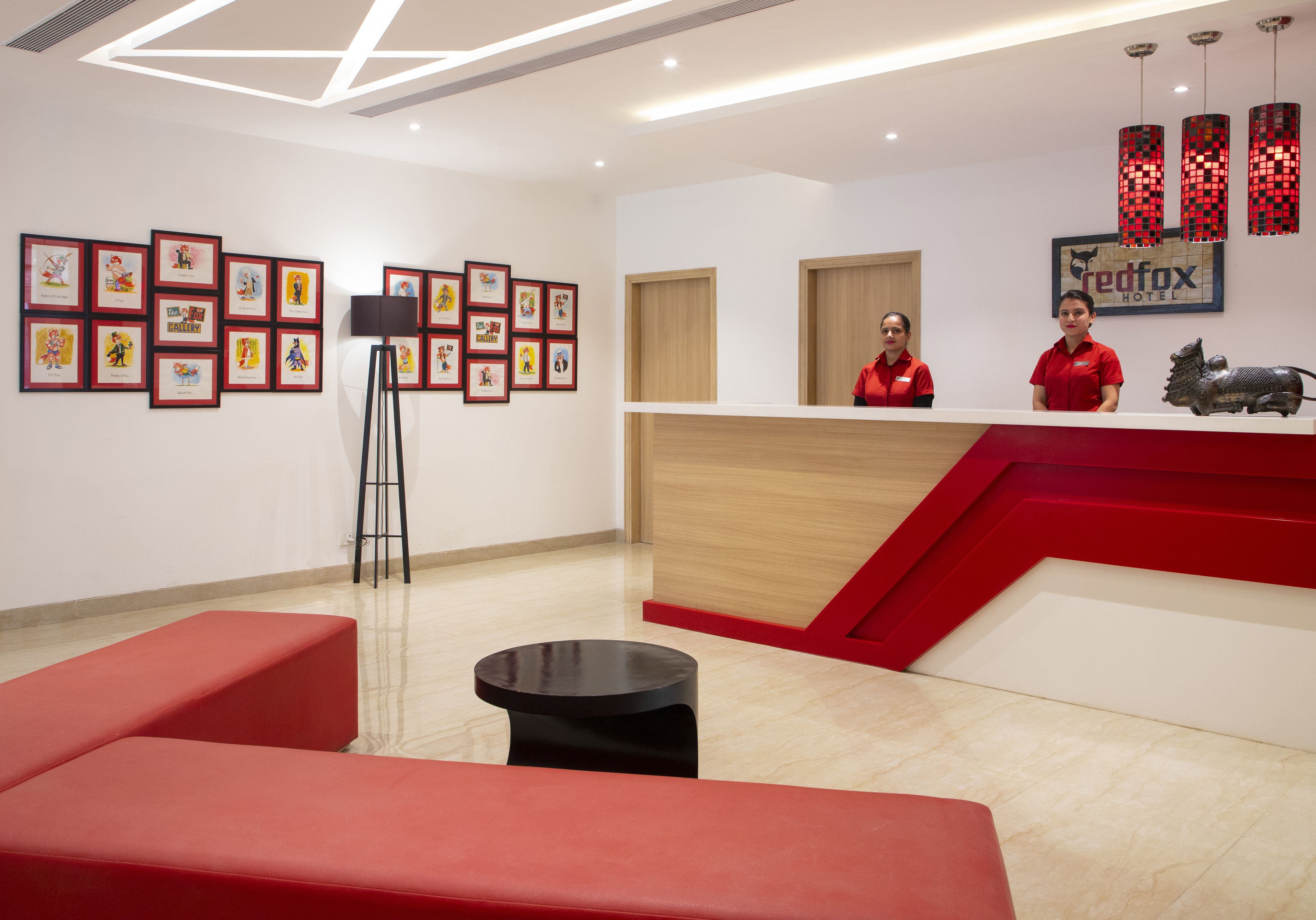 Un espace d’accueil d’hôtel aux couleurs rouge et blanche, avec des œuvres d’art encadrées accrochées aux murs et un comptoir de réception.
