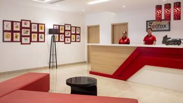 Un espace d’accueil d’hôtel aux couleurs rouge et blanche, avec des œuvres d’art encadrées accrochées aux murs et un comptoir de réception.