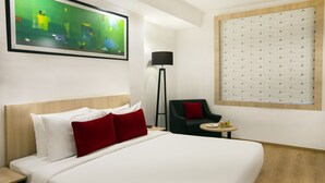 Une chambre d’hôtel avec un grand lit, une chaise, une petite table, une lampe sur pied et un tableau au mur.