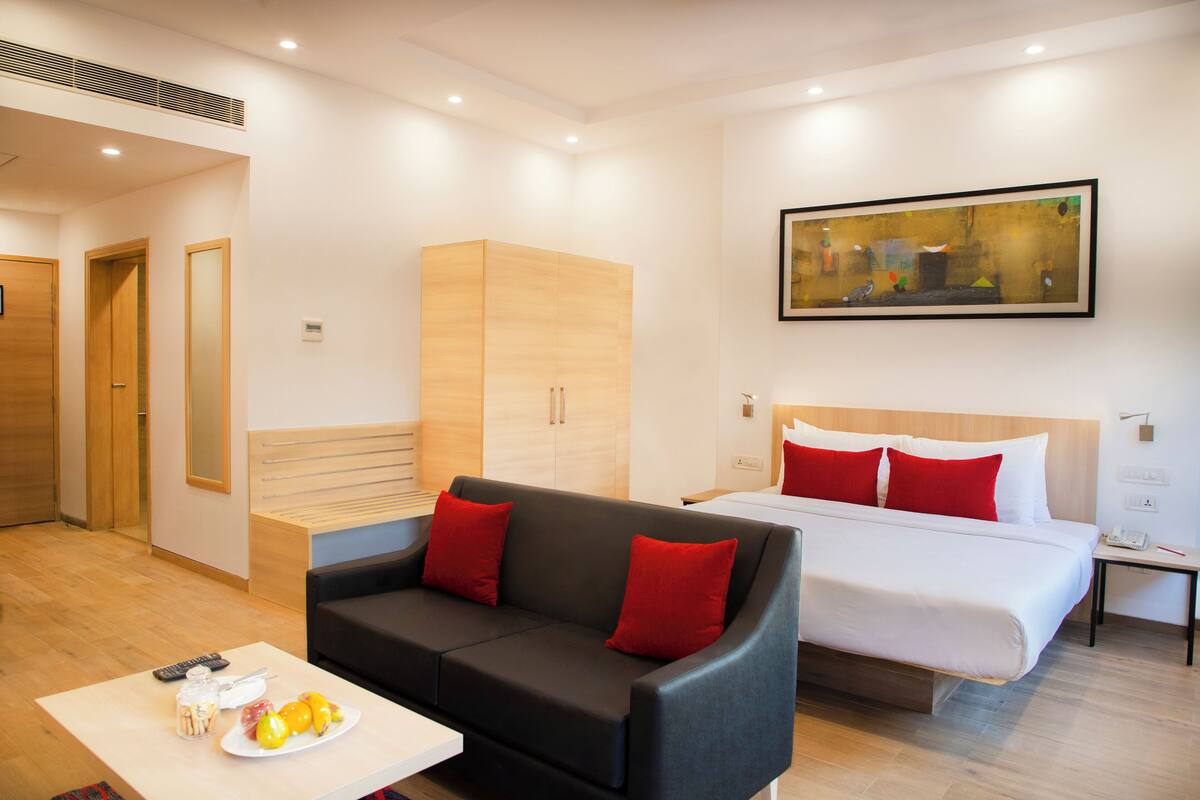 Een moderne hotelkamer met een bed, een bank, een nachtkastje, een schilderij en een fruitschaal op een bijzettafeltje.