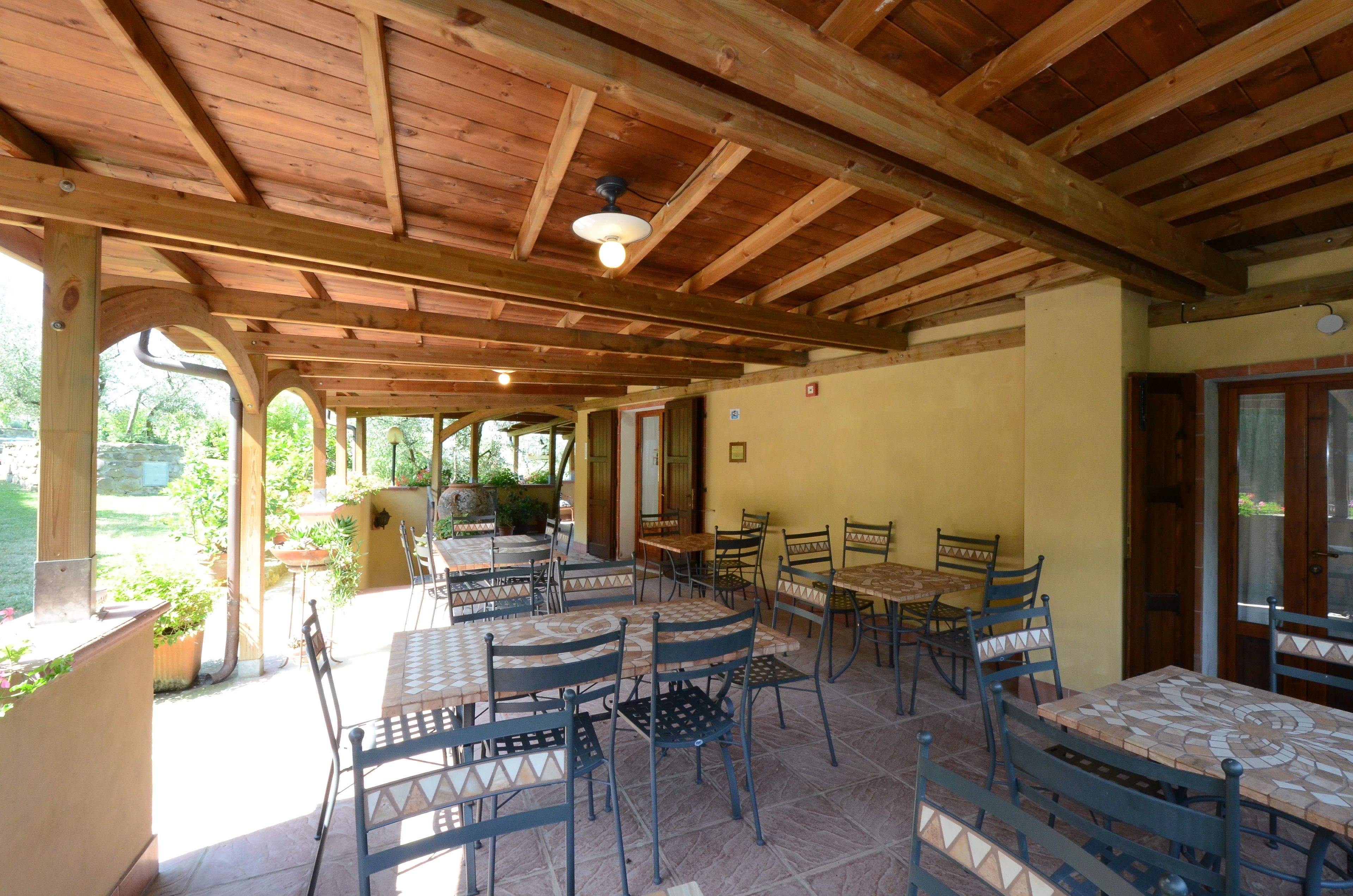 An outdoor patio with wooden beams, tiled flooring, and multiple tables and chairs.