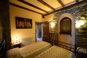 Quarto com duas camas, parede de pedra, porta de madeira, um quadro e um radiador.