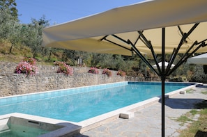 A swimming pool with a stone wall and flowers, surrounded by a stone patio and a large umbrella. - Agriturismo La Casella (Castelfranco Piandisco)
