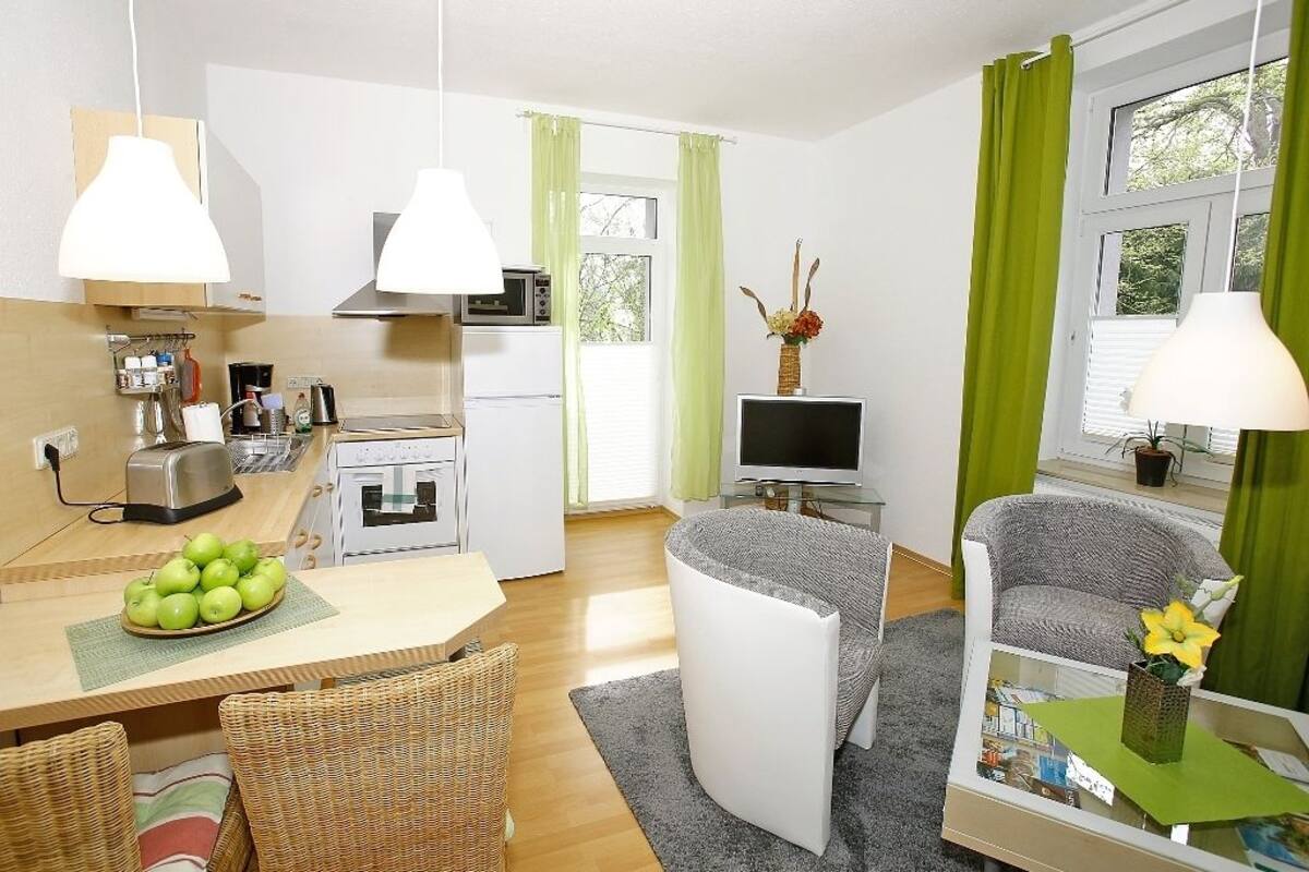 Un espace de vie compact comprenant un coin cuisine, un coin repas avec un panier de pommes, un canapé et un téléviseur.