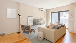 Uma sala de estar moderna com um sofá, uma poltrona, uma televisão e um abajur.