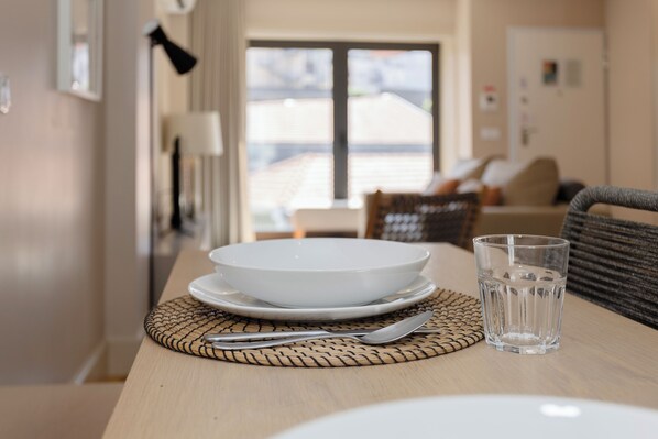 A dining table with a bowl, a glass, and cutlery on a woven placemat. - Liiiving In Porto Luxury Boutique Apart (Porto)