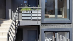 Edifício moderno com escada que leva a uma varanda com plantas, uma janela grande e um portão de metal.