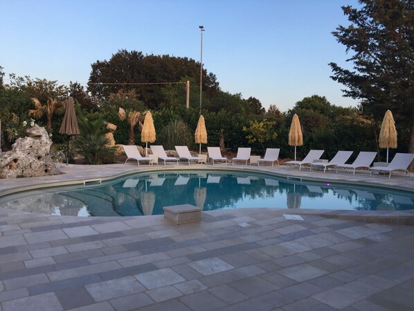 A swimming pool with lounge chairs and umbrellas, surrounded by greenery and a stone pathway. - Hotel Ristorante Punto Verde (Noci)