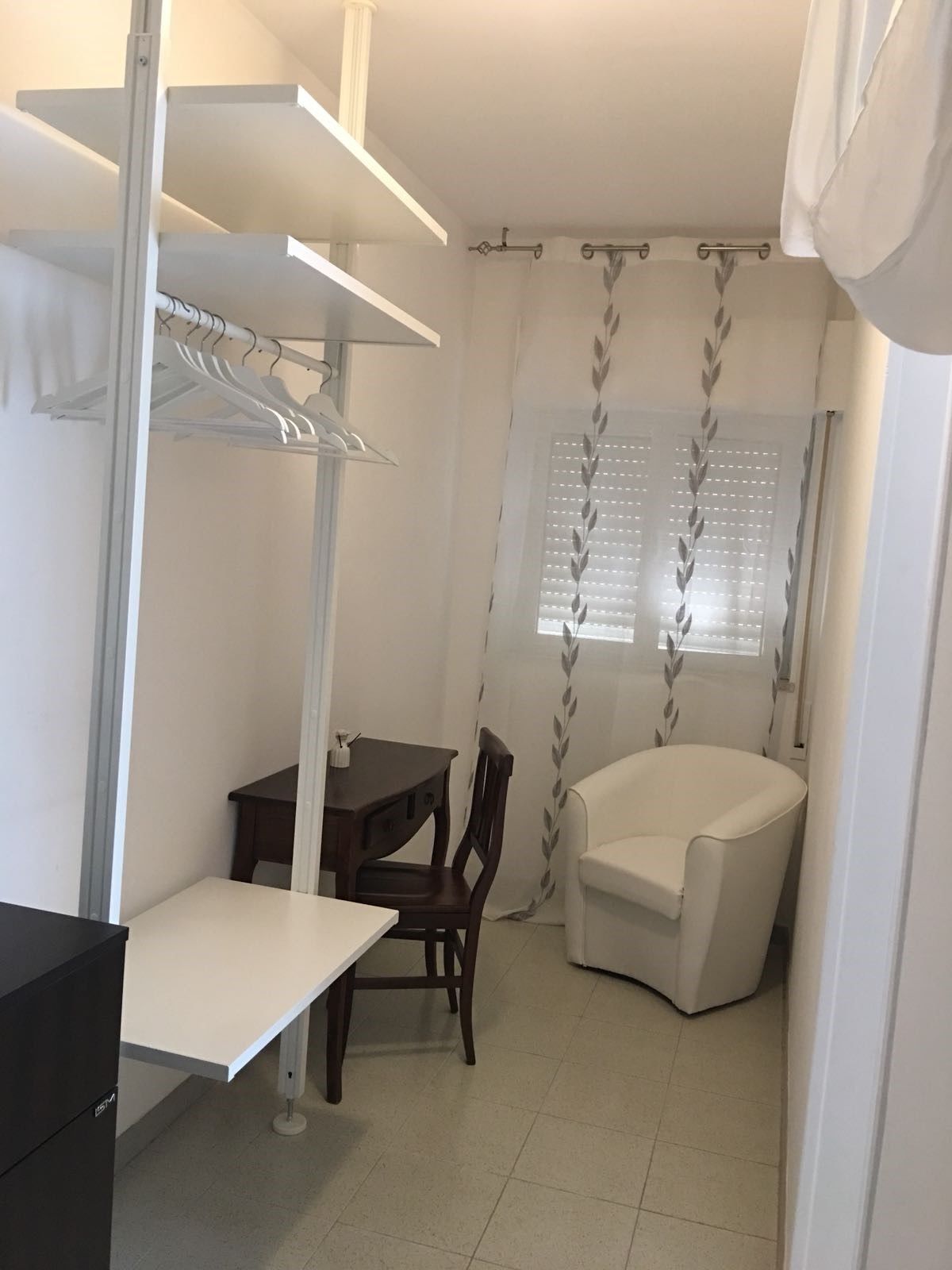 Una habitación compacta con una mesa de comedor, una silla, un sillón blanco y un armario con estantes.
