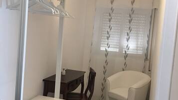 Una habitación compacta con una mesa de comedor, una silla, un sillón blanco y un armario con estantes.