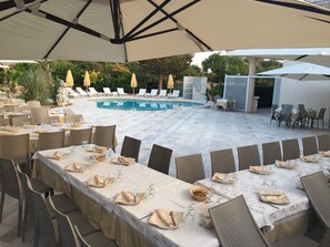 An outdoor dining area with tables set for a meal, a pool, and lounge chairs in the background. - Hotel Ristorante Punto Verde (Noci)