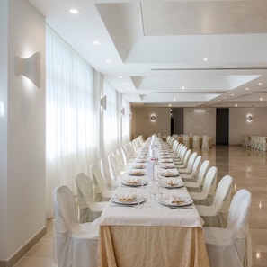 A long banquet table set for a formal event, with white chairs and a marble tablecloth.