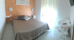 A bedroom with a bed, a bedside table, a chair, and a decorative wall piece. - Hotel Ristorante Punto Verde (Noci)
