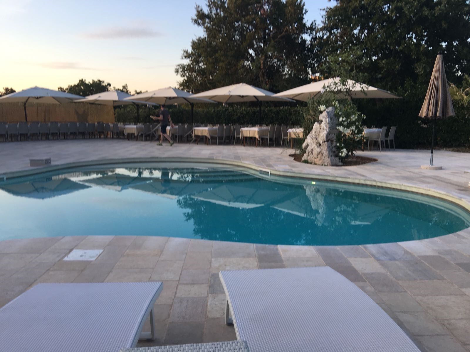 Una piscina con sillones de playa y sombrillas, rodeada de mesas y sillas.